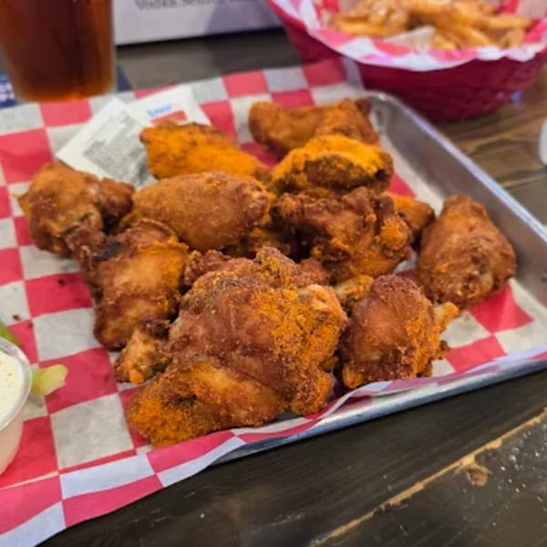 A metal tray of crispy, golden-brown chicken wings dusted with orange seasoning, served on red and white checkered paper.
