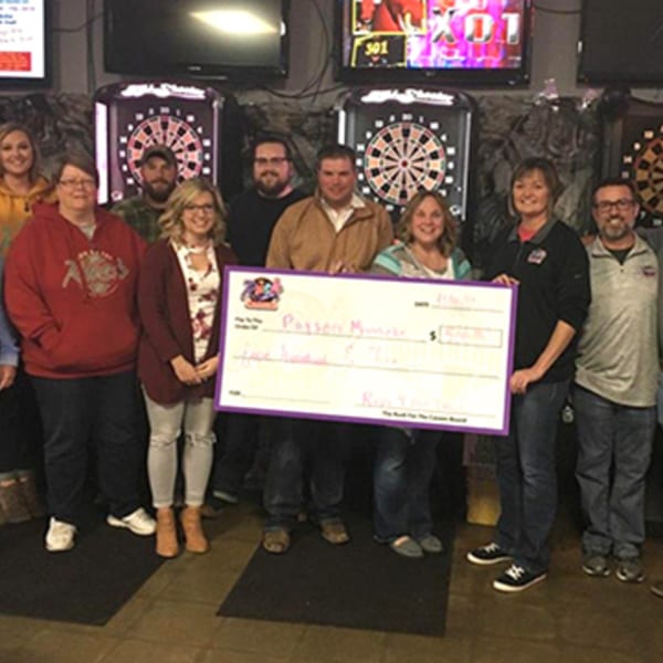 Group of ten people holding a large check, standing in front of dartboards at The Rush Bar & Grill.