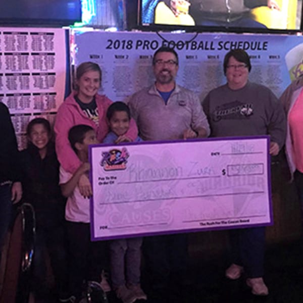 A group of adults and children smiling and holding a large check for "The Rush for the Causes Board".