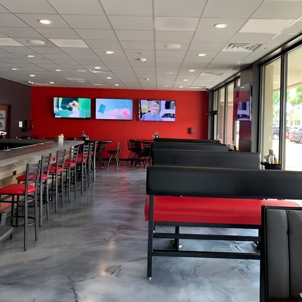 Interior of The Rush Bar & Grill with red walls, bar seating, booths, and multiple TVs.