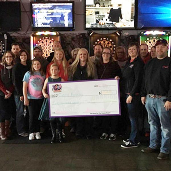 A group of people, including children, holding a large check at The Rush Bar & Grill.