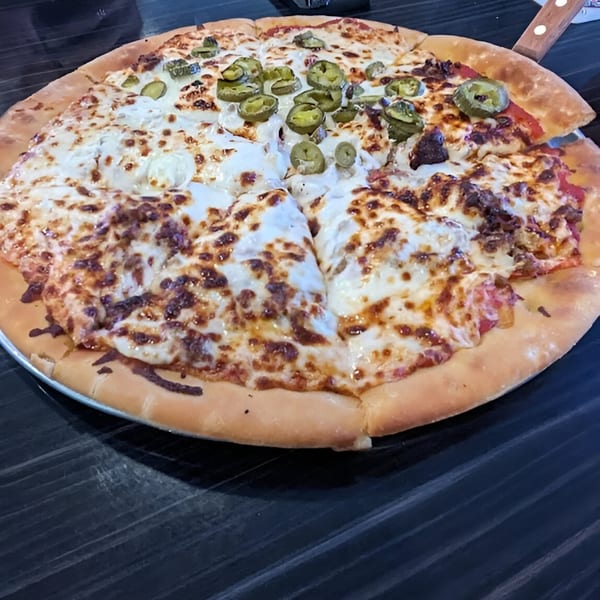 A large, round pizza with melted cheese, jalapeños, and meat, on a dark table.