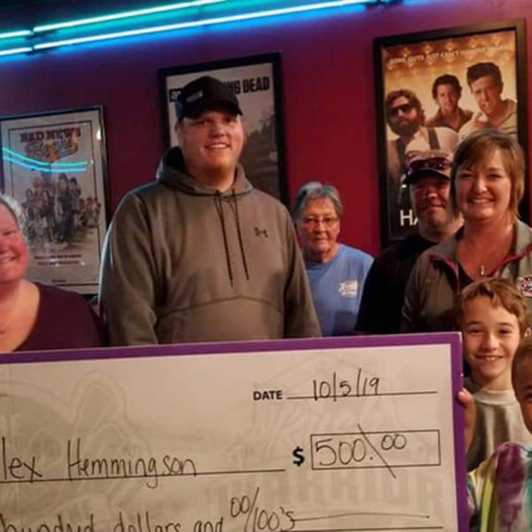 A group of smiling people, including children, holding a large check for $500.00 at The Rush Bar & Grill.