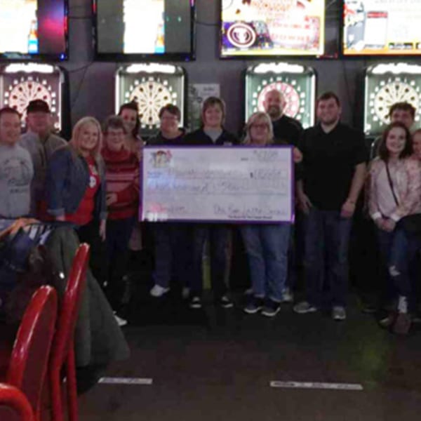 A group of people holding a large check in front of dartboards at The Rush Bar & Grill.