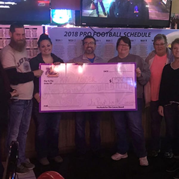 Six people from The Rush Bar & Grill holding a large check for "The Rush for the Causes".