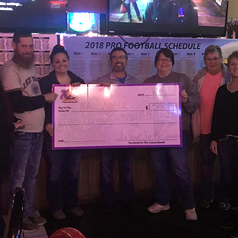 Six people from The Rush Bar & Grill holding a large check for "The Rush for the Causes".