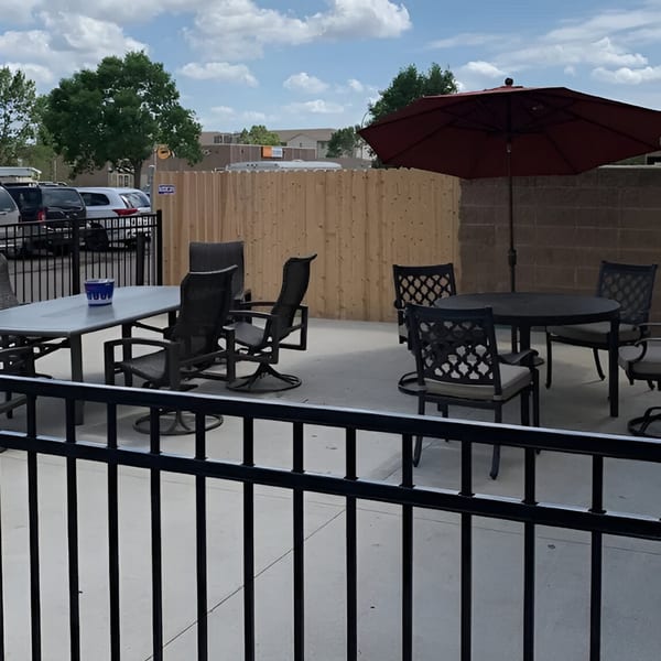 Outdoor patio at The Rush Bar & Grill with tables, chairs, and a large red umbrella.