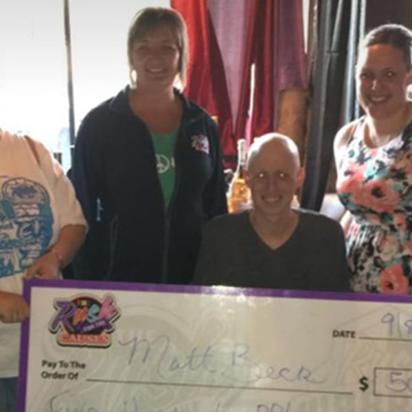 Four smiling people from The Rush Bar & Grill holding a large check for "Rush for the Causes".