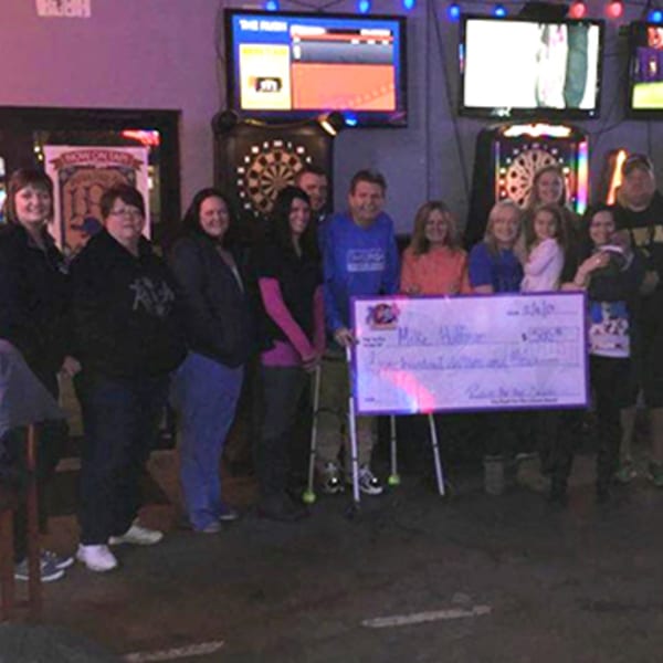 A group of people holding a large check for $500 inside The Rush Bar & Grill.