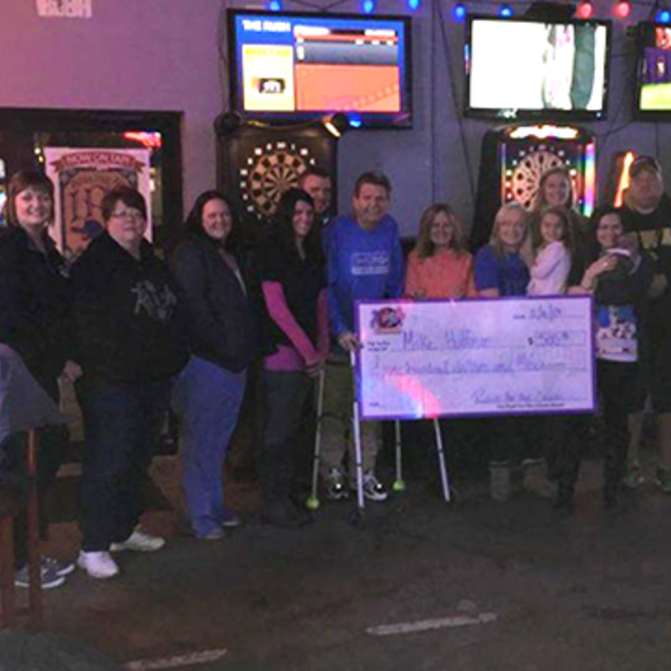 A group of people holding a large check for $500 inside The Rush Bar & Grill.