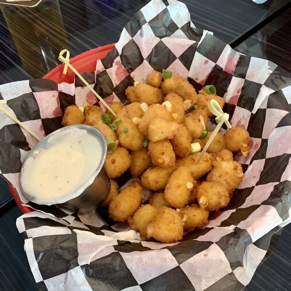 A basket of golden-brown cheese curds with green onions and a side of dipping sauce.