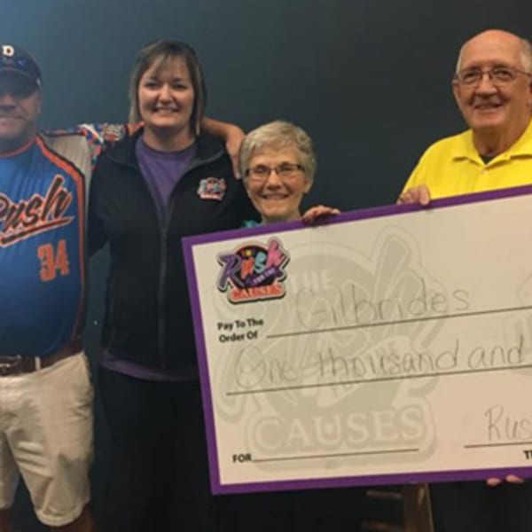 Four smiling people holding a large check from "Rush for the Causes" for "One thousand" dollars.