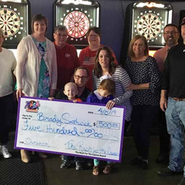 A group of people, including children, holding a large check for $500 in front of dartboards.