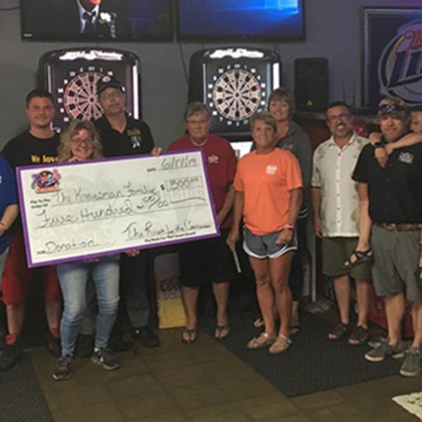 A group of people holding a large check for $500 in front of dartboards at The Rush Bar & Grill.