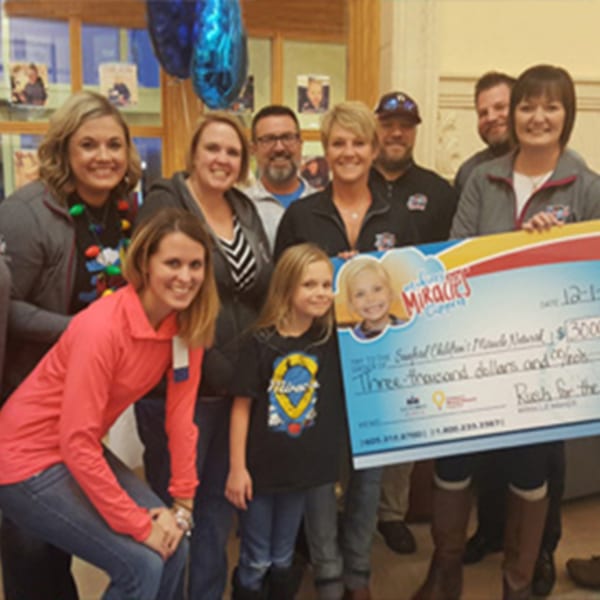 A group of adults and two children from The Rush Bar & Grill holding a large check for $3,000.