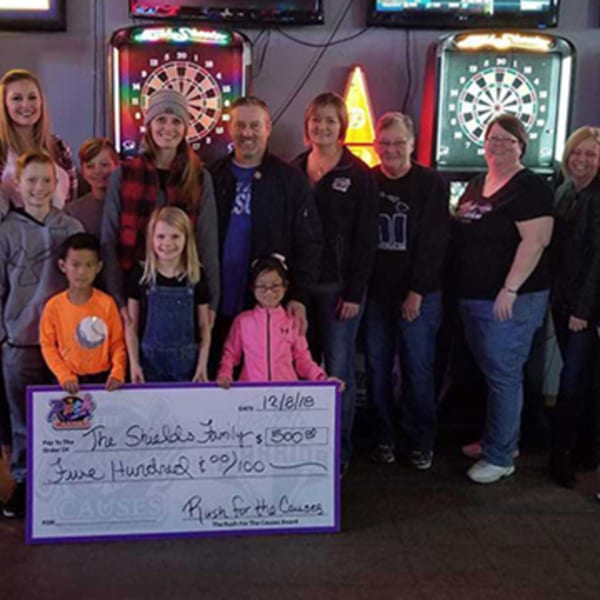 A group of adults and children holding a large check for "Rush for the Causes" at The Rush Bar & Grill.