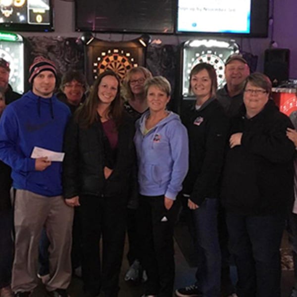Group of people posing for a photo in front of dartboards at The Rush Bar & Grill.