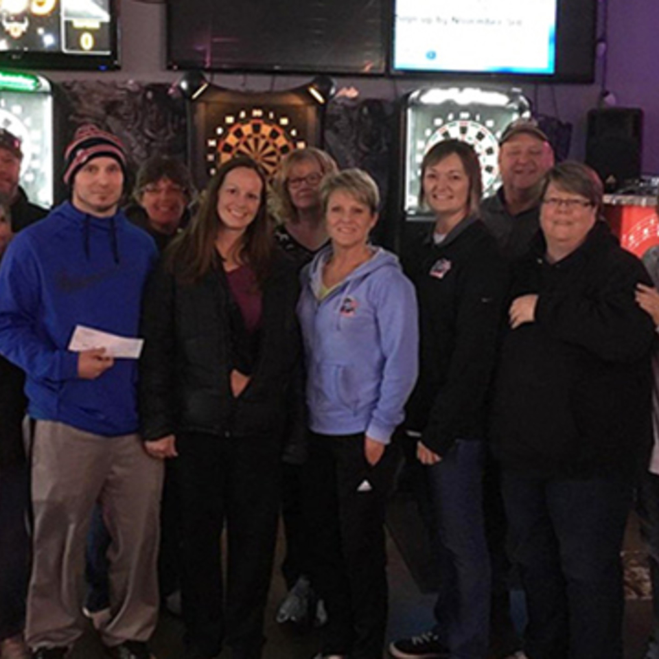 Group of people posing for a photo in front of dartboards at The Rush Bar & Grill.