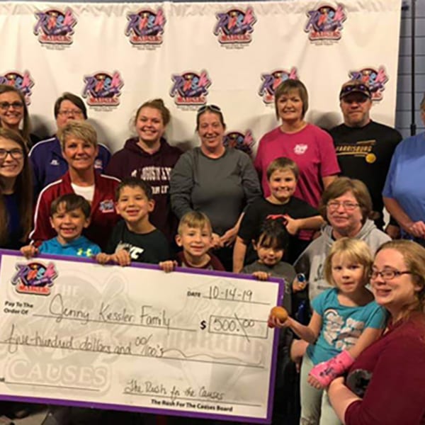 A group of adults and children holding a large check for $500, "The Rush for the Causes" event.
