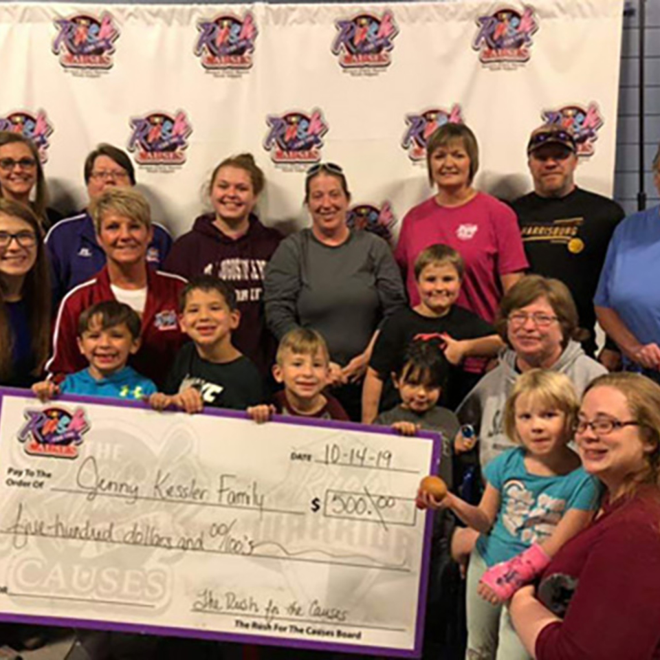 A group of adults and children holding a large check for $500, "The Rush for the Causes" event.