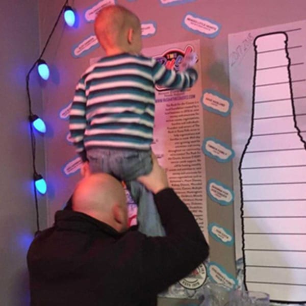 A man holds a child up to place a sticker on a large poster at The Rush Bar & Grill.