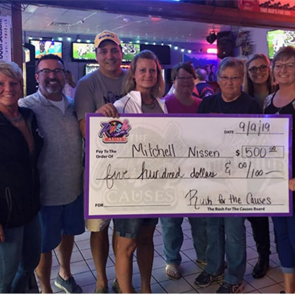 A group of people holding a large check for $500 made out to Mitchell Nissen from Rush for the Causes.