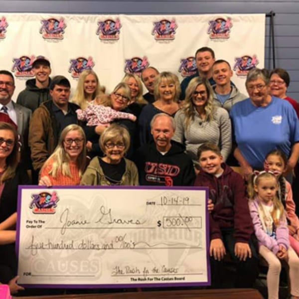 A large group of people, including children, pose with a giant check for "The Rush for the Causes."