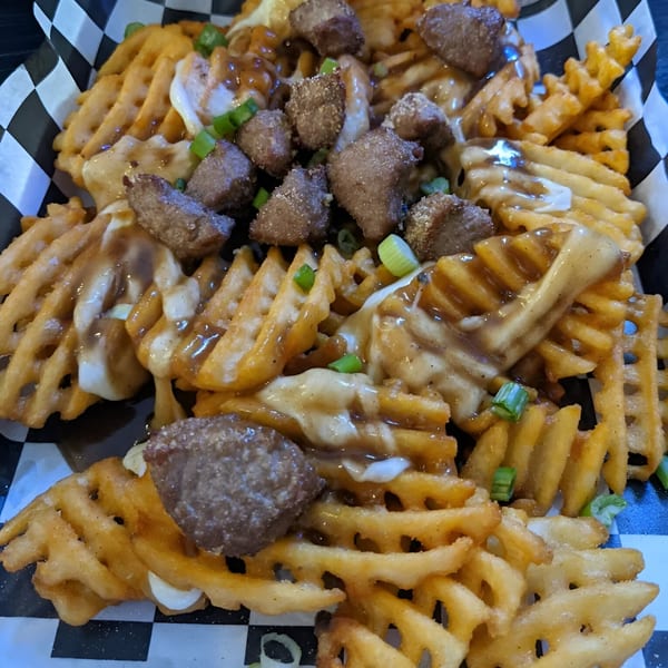 Waffle fries topped with gravy, cheese curds, steak bites, and green onions in a checkered basket.