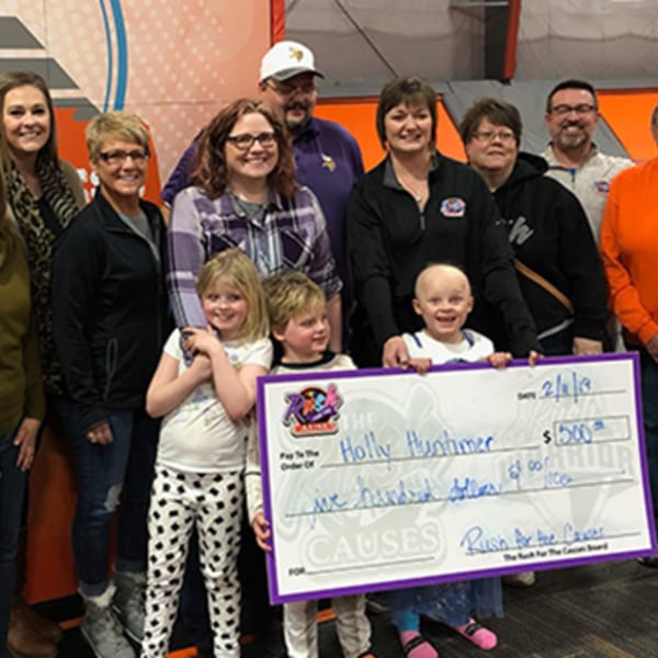 A group of adults and children holding a large check for $500 made out to Holly Huntimer.
