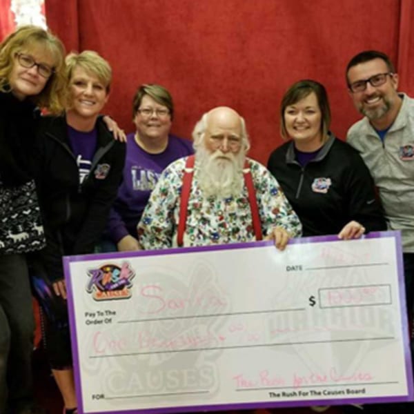 Six people, including a Santa Claus look-alike, holding a large check for "Rush for the Causes."