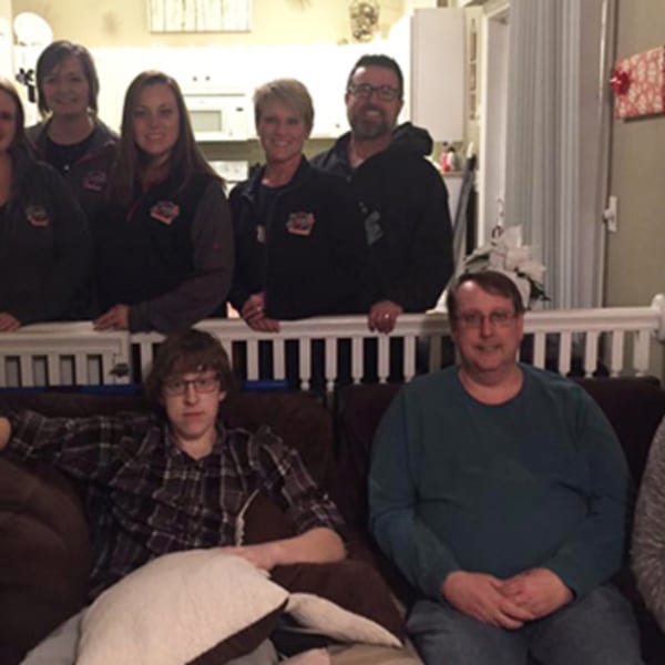 Six smiling Rush Bar & Grill staff members stand behind two men seated on a couch.