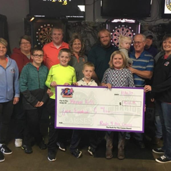 A group of adults and children holding a large check for "Happy Kids" at The Rush Bar & Grill.