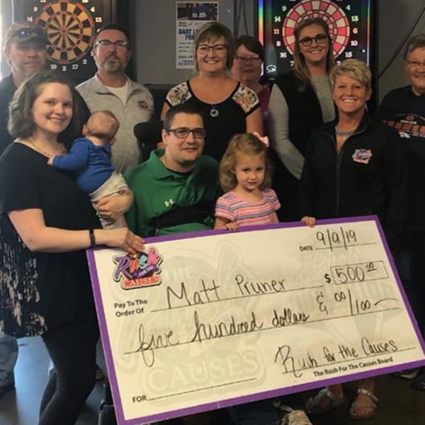 A group of people, including children, holding a large check for "Rush for the Causes" at The Rush Bar & Grill.