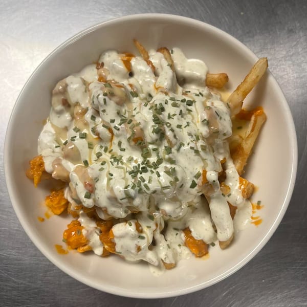 A white bowl of The Rush Bar & Grill's fries topped with creamy sauce, buffalo sauce, and chives.