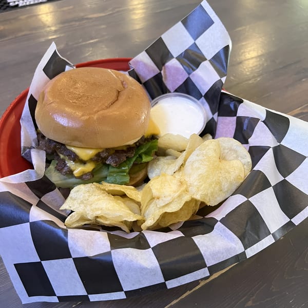 A double cheeseburger with lettuce, chips, and a side of ranch in a red basket with checkered paper.