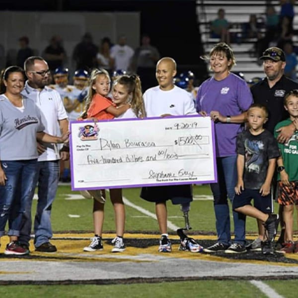 A group of adults and children on a football field holding a large check for Dylan Bourassa.