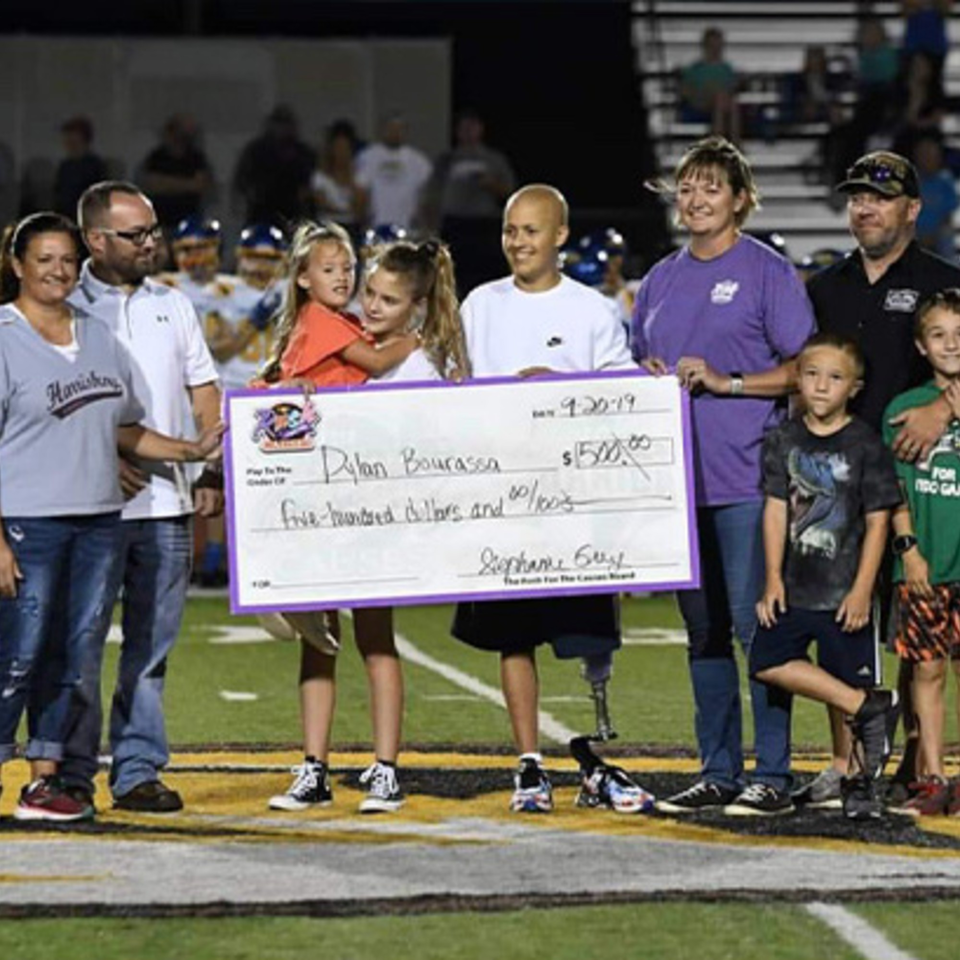A group of adults and children on a football field holding a large check for Dylan Bourassa.