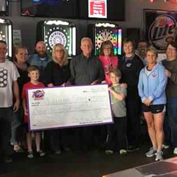 A group of people, including children, holding a large check at The Rush Bar & Grill.