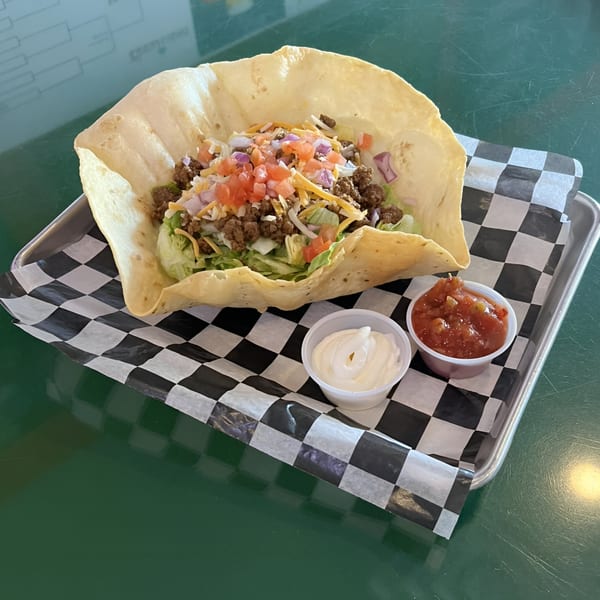 A taco salad in a large fried tortilla bowl with ground beef, lettuce, cheese, and tomatoes.