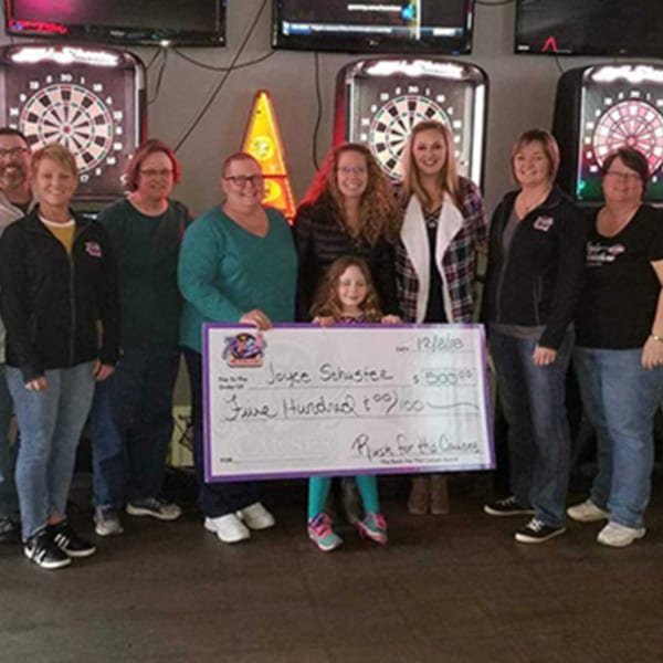 A group of adults and one child holding a large check for "Rush for the Causes" in a bar.