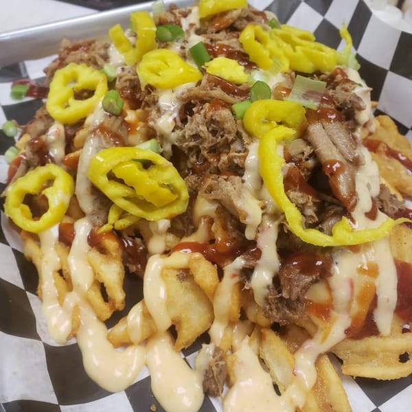 Loaded fries from The Rush Bar & Grill, topped with pulled pork, cheese sauce, BBQ sauce, and peppers.